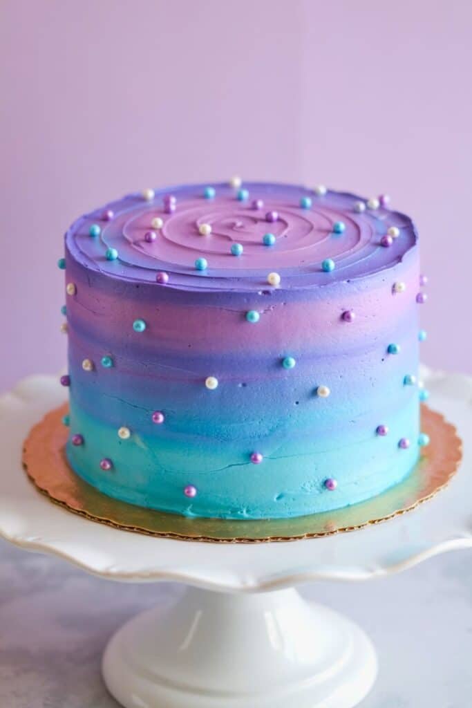 Elegant mermaid birthday cake with purple, pink, and teal ombre frosting, decorated with pearl sprinkles; perfect simple cake idea for a mermaid-themed birthday party.  