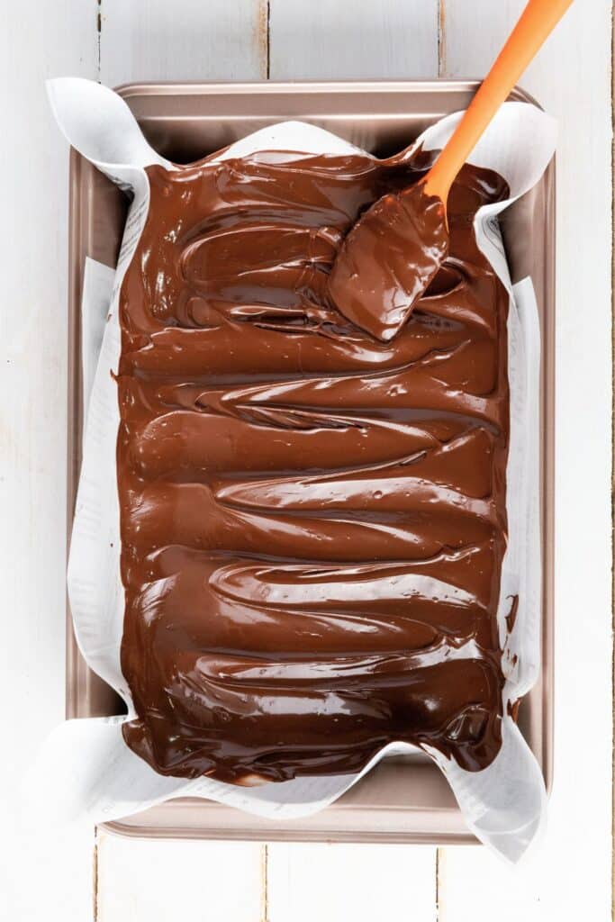 Melted dark chocolate spread in an even layer with a spatula inside a parchment-lined baking pan. Step in the process of making patriotic chocolate bark for a fun and easy 4th of July dessert.