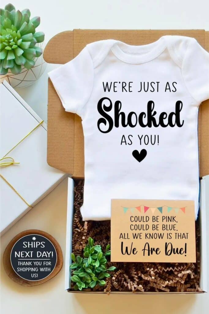 Unexpected pregnancy announcement box with baby onesie that says 'We’re just as shocked as you!' and card that reads 'Could be pink, could be blue, all we know is that we are due!