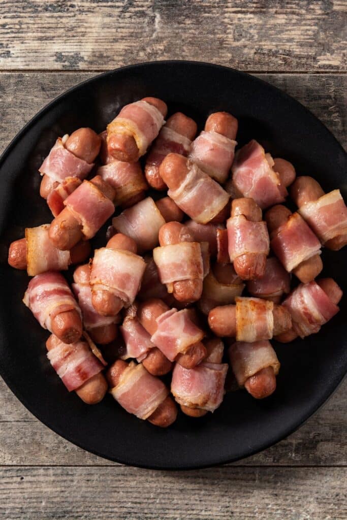 Bacon-wrapped little smokies arranged on a black plate. A savory, crowd-pleasing party appetizer that’s easy to make and perfect for birthday parties, baby showers, or game day gatherings.