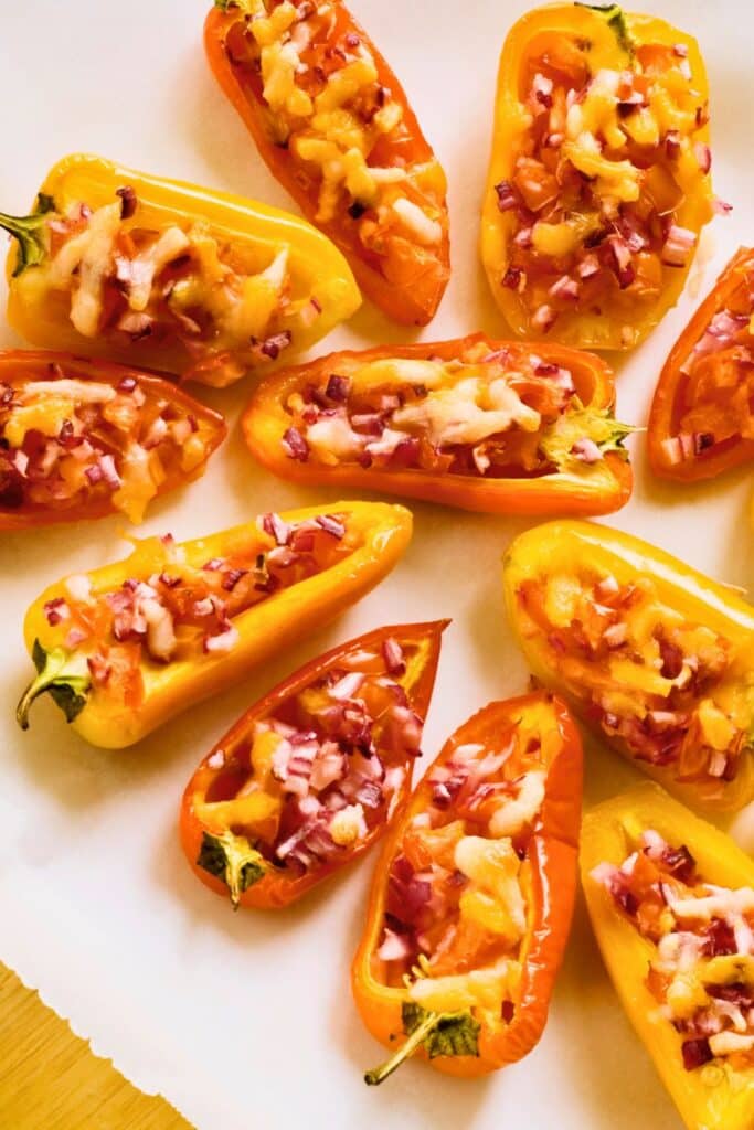 Stuffed mini bell peppers baked with melted cheese and diced red onion, arranged on parchment paper. A colorful and bite-sized appetizer perfect for baby showers, birthday parties, or holiday gatherings.