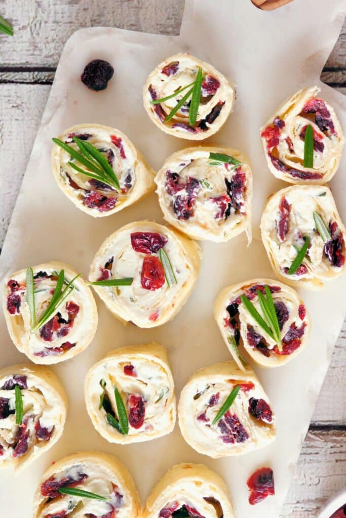 Tortilla pinwheels filled with cream cheese, dried cranberries, and fresh herbs, arranged on a marble cutting board. A festive, make-ahead party appetizer perfect for baby showers, birthday parties, or holiday gatherings.