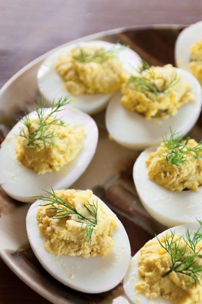 Classic deviled eggs garnished with fresh dill on a ceramic platter. A simple and elegant appetizer perfect for baby showers, holiday gatherings, or birthday party spreads.