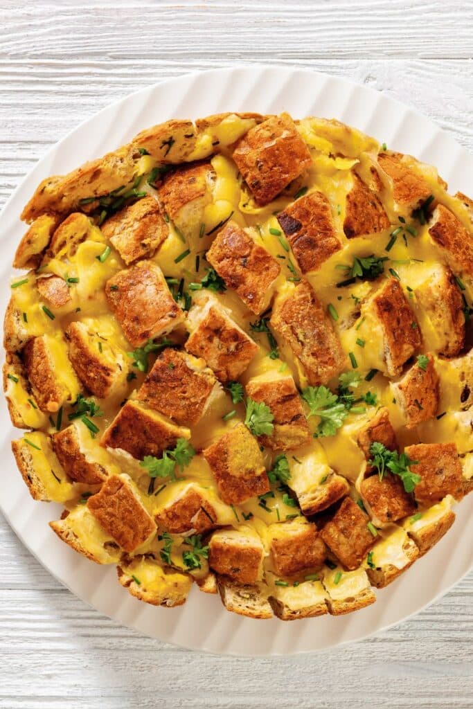 Cheesy pull-apart bread topped with melted cheese and herbs, served on a white plate. A warm, crowd-pleasing appetizer perfect for baby showers, birthday parties, or cozy holiday gatherings.