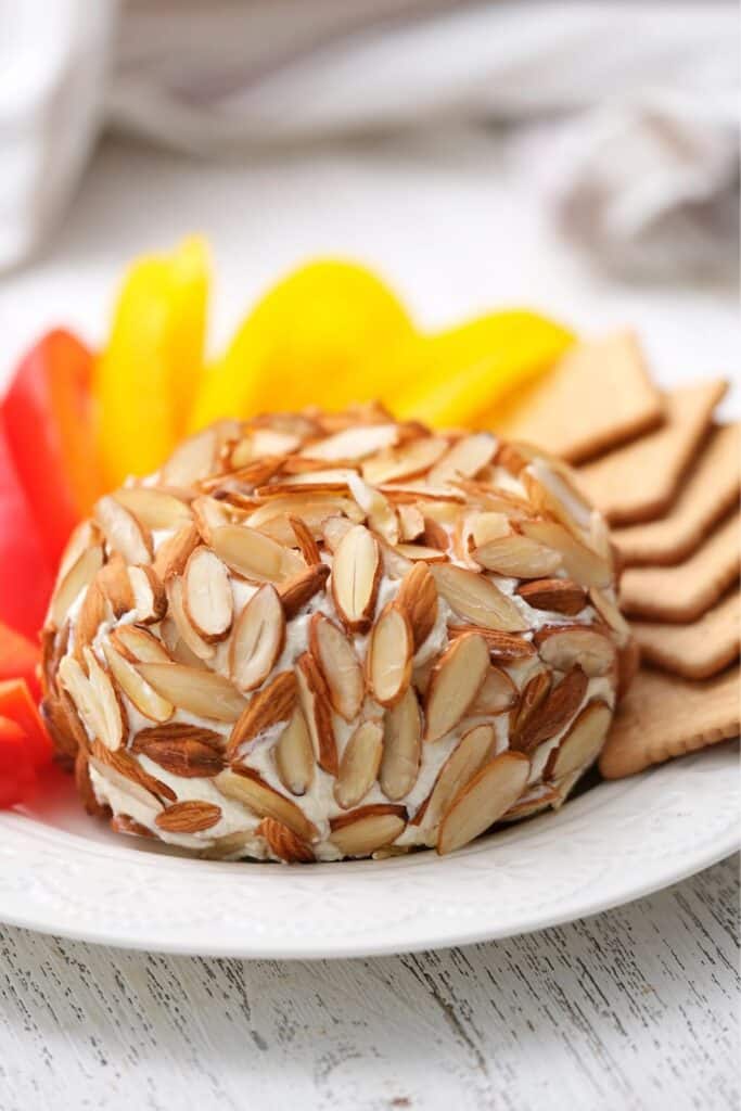 Almond-crusted cheese ball served with sliced bell peppers and crackers on a white plate. A make-ahead appetizer that’s elegant, easy, and perfect for baby showers, holiday parties, or birthday celebrations.