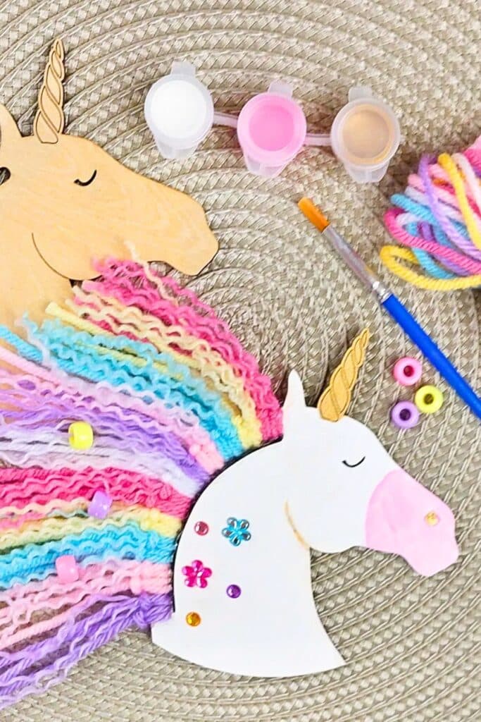 Unicorn craft activity with wooden unicorn cutouts, pastel yarn manes, colorful beads, paint pots, and a brush — a fun and creative DIY station idea for a unicorn-themed birthday party.