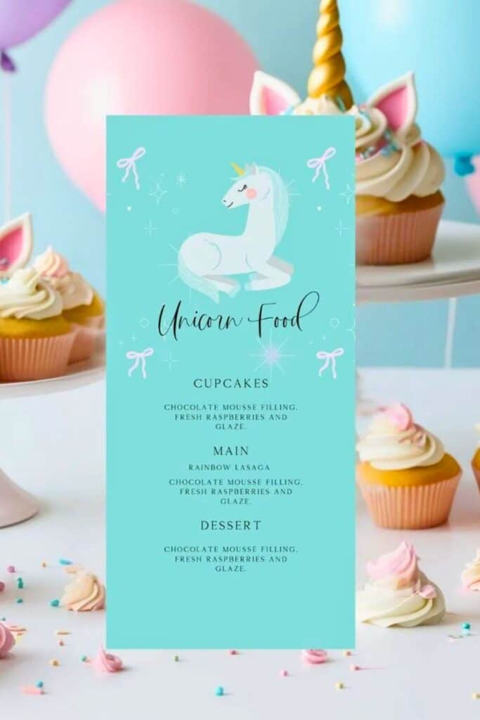 Unicorn birthday party food menu displayed on a pastel blue sign with a white unicorn illustration, surrounded by cupcakes with unicorn toppers and pink balloons — a whimsical and coordinated food table setup.