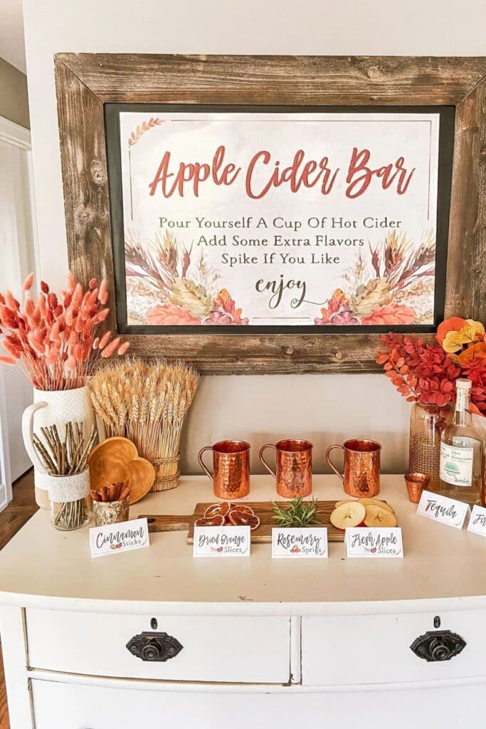 Apple cider bar for fall baby shower with copper mugs, apple cider toppings, cinnamon sticks, and bourbon setup — cozy apple of my eye baby shower drink station.