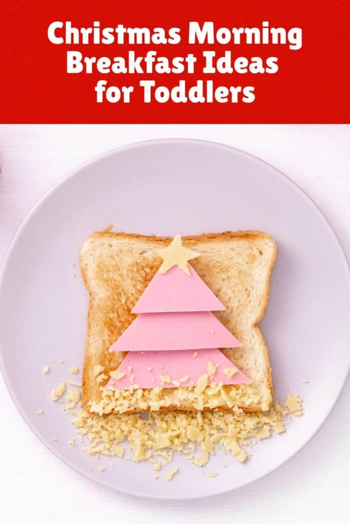 A slice of toast decorated to look like a Christmas tree, made with stacked pink ham triangles and topped with a star-shaped cheese slice. Shredded cheese is sprinkled at the bottom to resemble snow, and the plate is surrounded by festive holiday decor like ribbons and a mini tree.