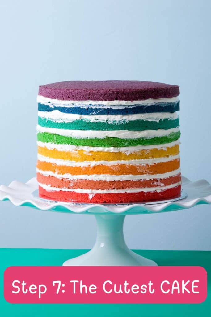 Colorful rainbow layer cake with white frosting on a pedestal stand for a toddler girl’s 2nd birthday party.  