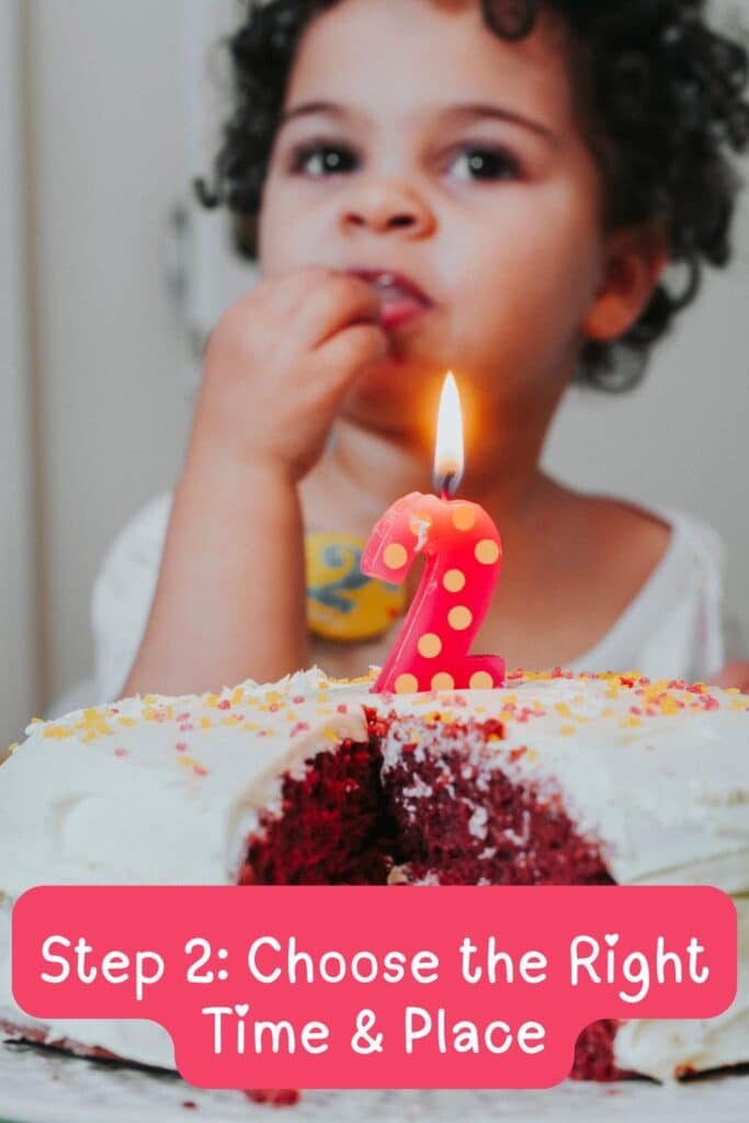 Toddler girl eating cake with a pink number 2 candle lit in front of her during her second birthday party.