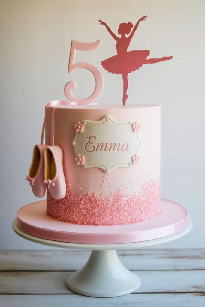 Pink ballerina-themed 5th birthday cake with sugar crystal sprinkles, fondant ballet slippers, and a silhouette ballerina topper on a white cake stand.