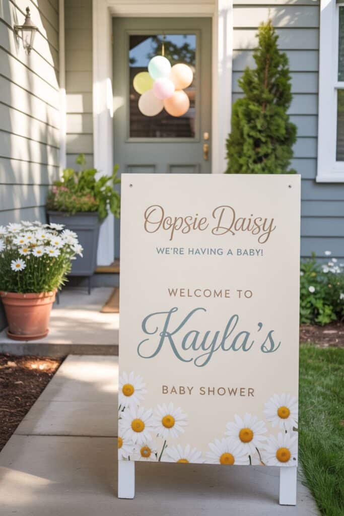 Daisy-themed welcome sign reading ‘Oopsie Daisy, we’re having a baby! Welcome to Kayla’s Baby Shower’ on a spring porch with potted daisies and pastel balloons.