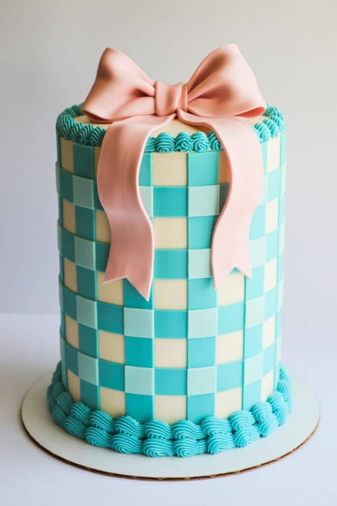 Tall teal gingham gender reveal cake with checkerboard fondant panels, blush pink bow topper, and piped teal buttercream border on a white cake board.