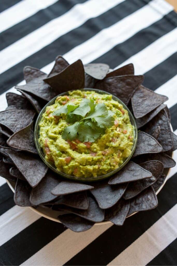 spooky baby shower food with guacamole and black tortilla chips for a we’ve created a monster halloween baby shower