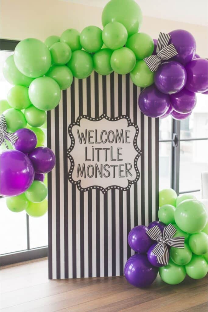 monster baby shower backdrop with green and purple balloon arch welcome little monster sign for a we’ve created a monster baby shower theme