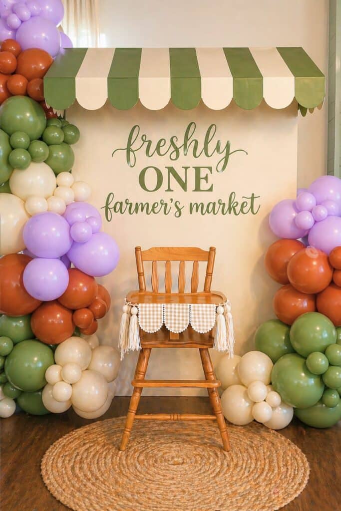 Freshly one farmer’s market first birthday backdrop with green striped awning, balloon garland, and high chair setup for a baby girl party