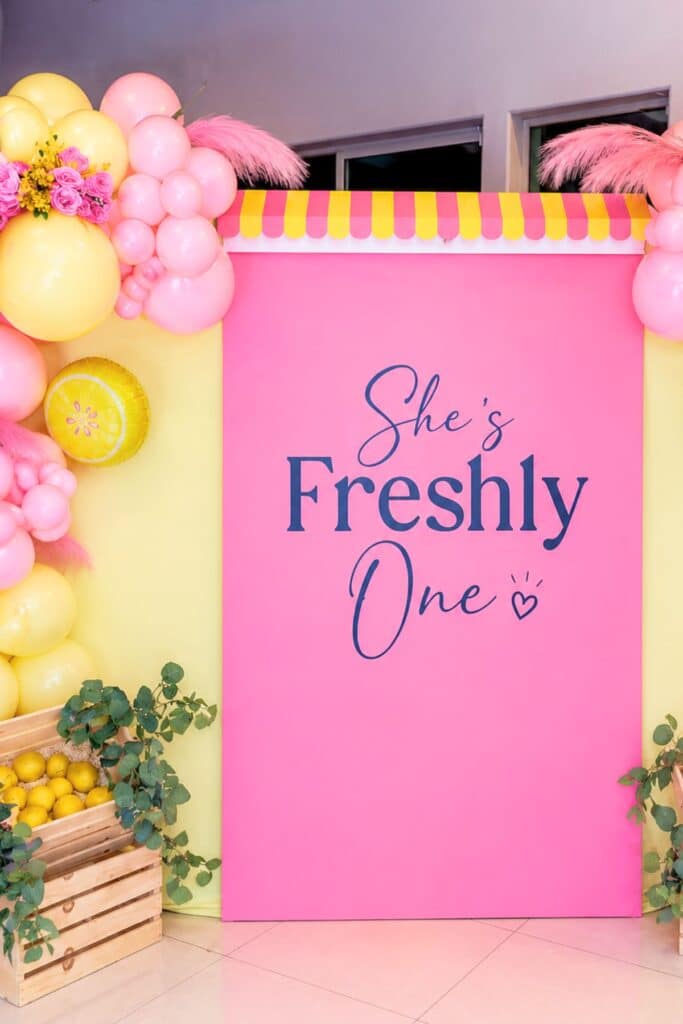 Freshly one first birthday party backdrop with pink and yellow balloon arch and “She’s Freshly One” sign for a baby girl party