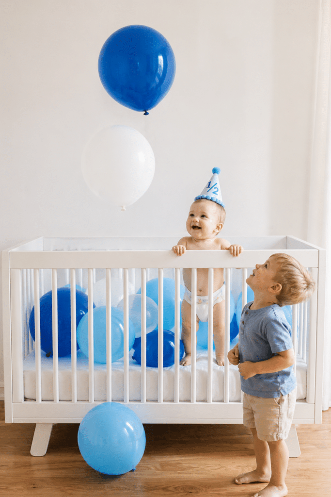 baby boy sitting in crib with 1/2 balloons for half birthday, simple 6 month milestone photo idea with neutral nursery setup