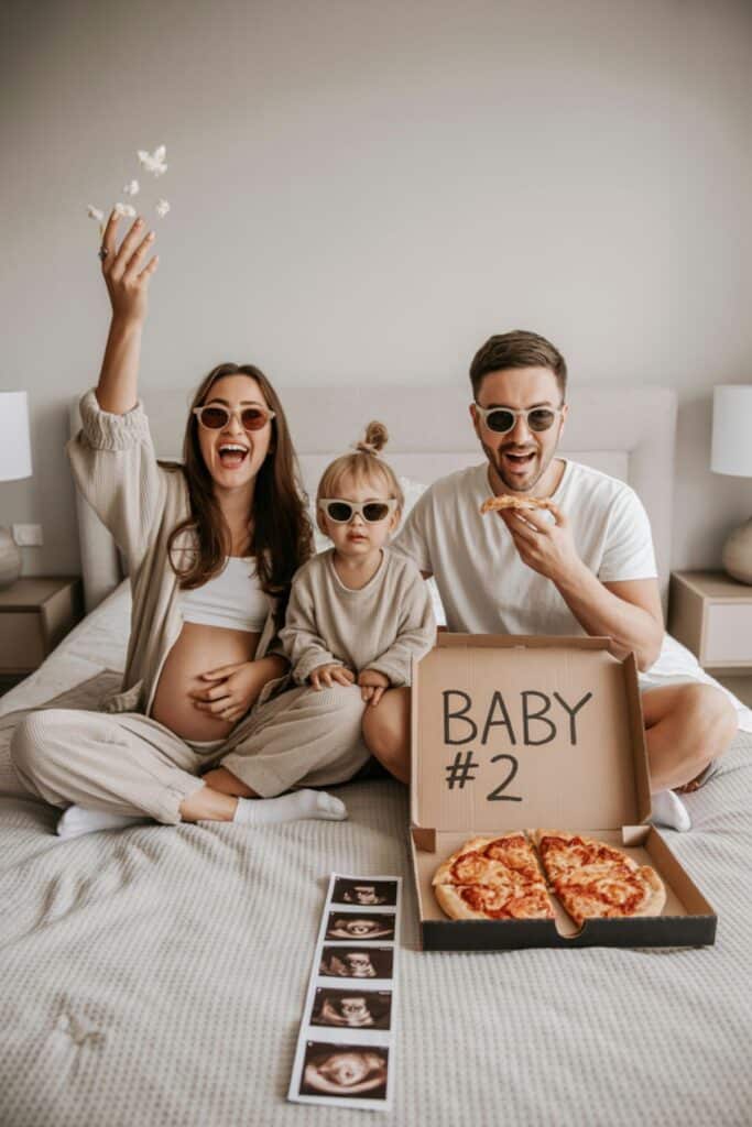 Family sitting with pizza box that says baby #2 for fun second pregnancy announcement idea with toddler and ultrasound photos