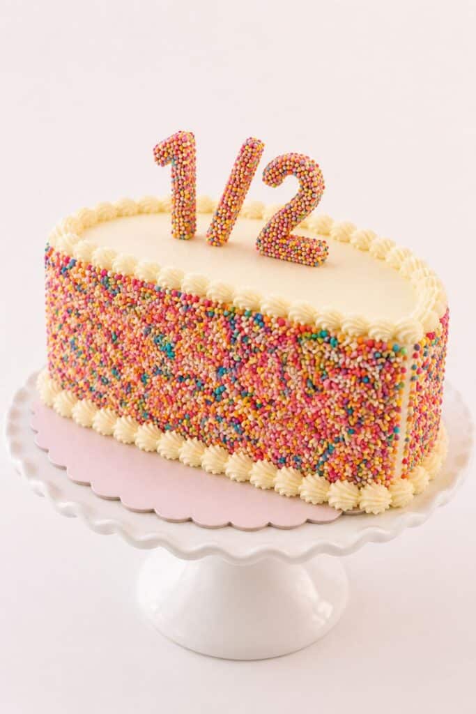 Colorful sprinkle-covered half birthday cake with “1/2” topper for a fun and bright 6 month birthday celebration idea.