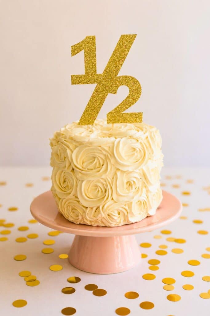 Elegant white rosette half birthday cake with gold “1/2” topper for a classy and simple 6 month birthday celebration.
