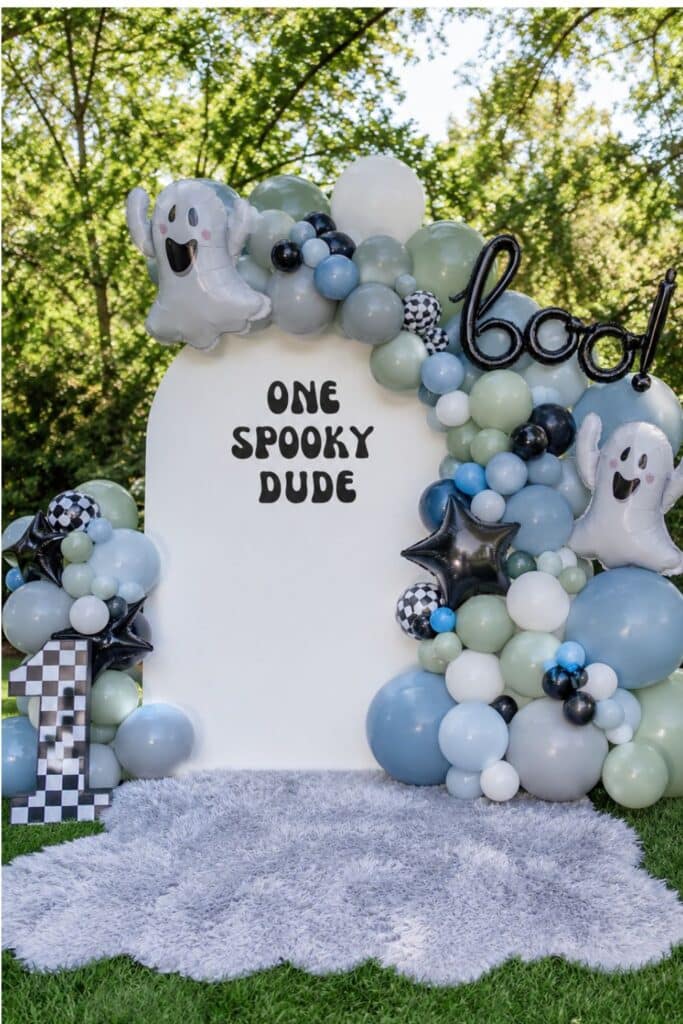 One Spooky Dude first birthday backdrop with blue, green, black, and white balloons, ghost decorations, and checkered number one.